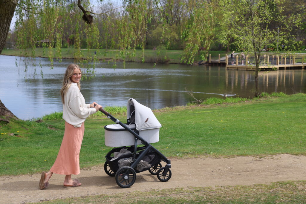 mom pushing her uppababy stroller on a trail with a pond and dock in the background